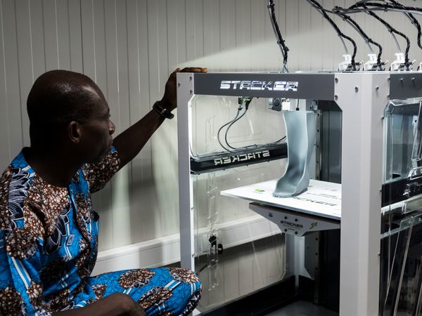Der Orthopäde Mathieu Afetse arbeitet an einer Orthese aus dem 3D Drucker. Er sitzt vor dem Drucker, in dem grade eine Orthese gedruckt wird