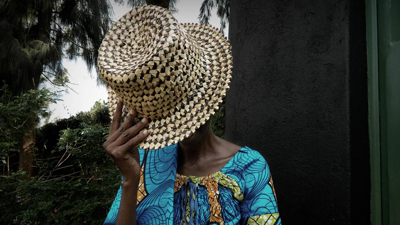 Eine Frau aus Ruanda hält sich beschämt den Strohhut vors Gesicht