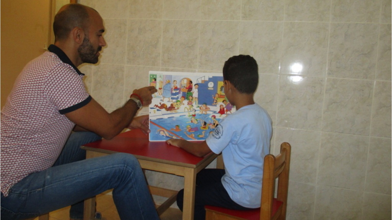 Ein Mitarbeiter von Handicap International führt mithilfe von Bildern Logopädietraining mit einem Kind durch.