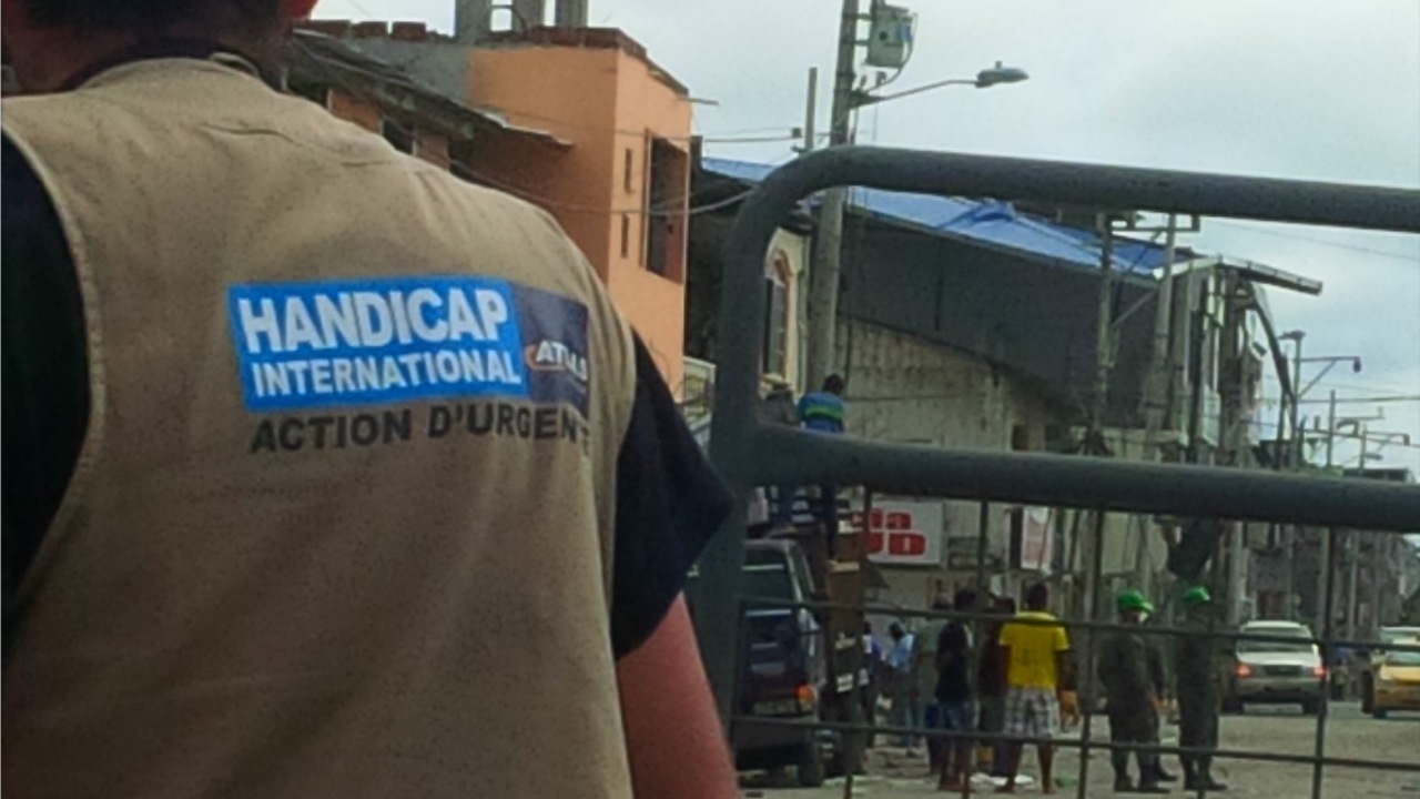 Ein Mitarbeiter von des Handicap International Notfall-Teams steht mit dem Rücken zur Kamera. Im Hintergrund ist eine Straßenszene zu sehen