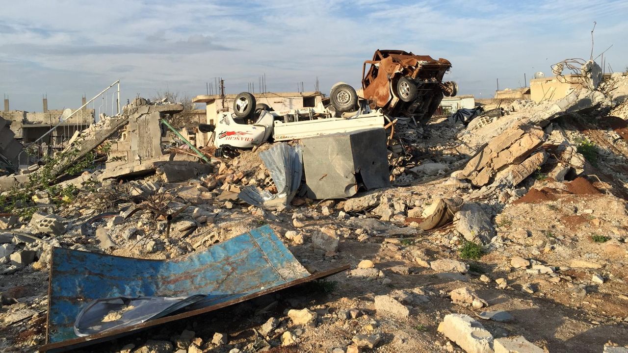 Man sieht Kobane nach der Bombardierung. Ein Trümmerfeld unter blauem Himmel. 