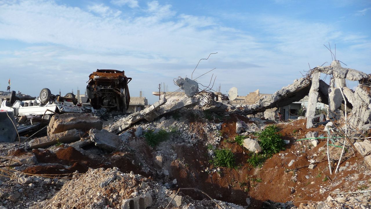 Ein Bombenkrater in der Stadt Kobane in Syrien. Im Hintergrund sind zwei umgedrehte Autos.