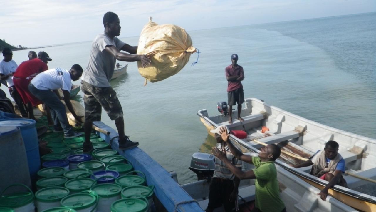 Männer verladen Säcke und Eimer mit Hilfsgütern in die Boote, die sie in schwer erreichbare Gegenden von Haiti bringen
