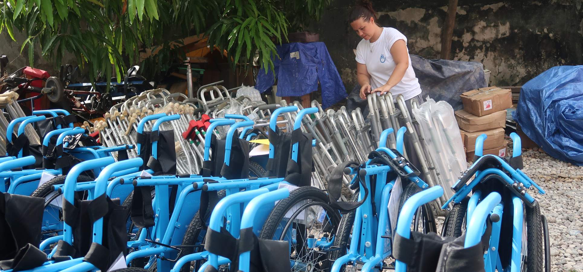 Eine Hilfslieferung hat die Haiti erreicht,. Viele Rollstühle sind am Strand abgelagert, im Hintergrund kümmert sich eine Mitarbeiterin von HI um die Lieferung.