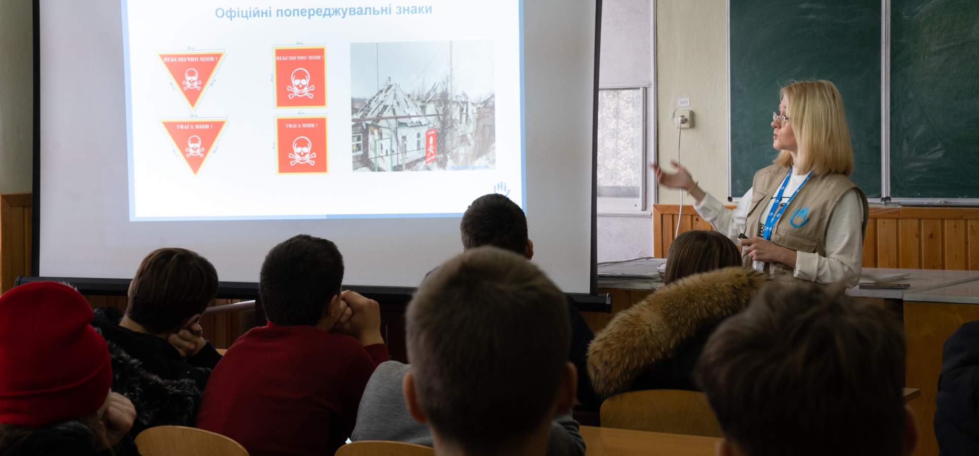 Bei einer Minenaufklärstunde in der Ukraine. Eine blonde Frau zeig den Kindern an der Tafel, worauf sie aufpassen müssen.