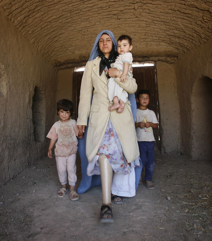 Frau, die eine Beinprothese trägt mit ihren Kindern in einer Lehmhütte