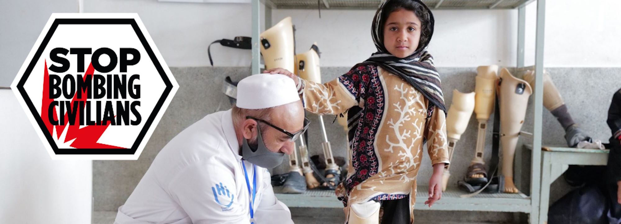 Ein kleines Mädchen in afghanischer Kleidung und ein HI-Physiotherapeut