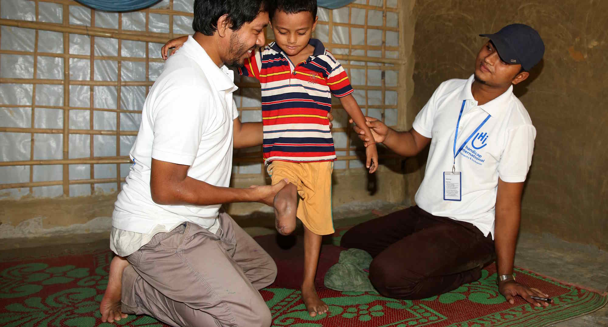Ein lächelnder HI-Physiotherapeut hält einen kleinen Junge auf dem Schoß; er hat nur ein Bein.