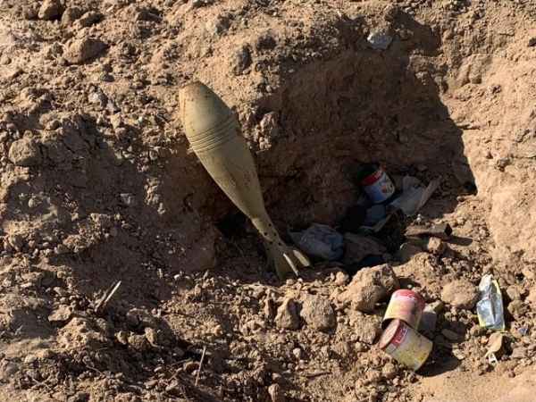 Ein Blindgänger liegt in einem Graben. Ringsherum liegen alte Konserven. 