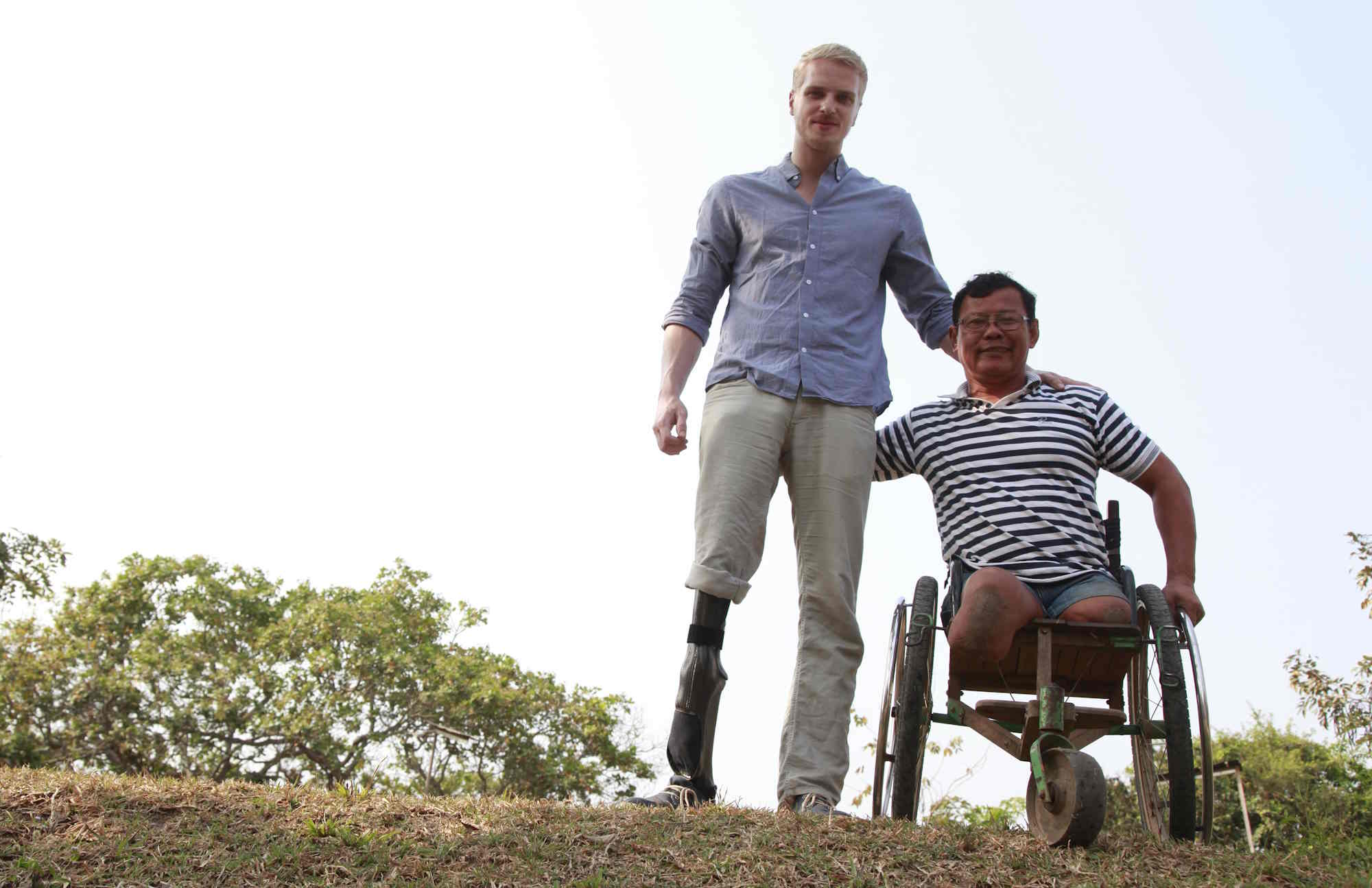 Zwei Männer nebeneinander. Ener hat ein künstliches Bein, er steht neben dem anderen Mann, der in einem Rollstuhl sitzt.