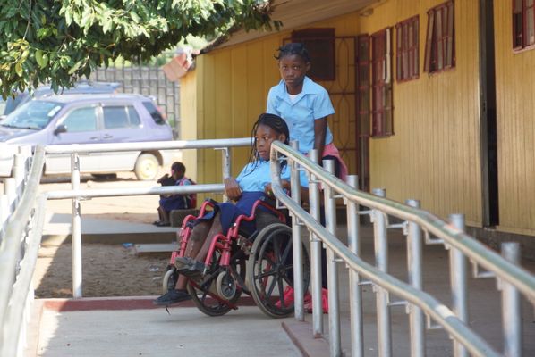 Chelsia im Rollstuhl wird von einer Freundin die Rampe zur Schule hinaufgeschoben