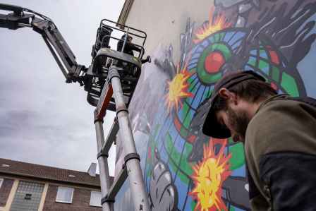 Graffiti Künstler AKUT sprüht sein Kunstwerk von einer Hebebühne aus in Augsburg.