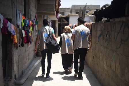 Drei Mitarbeiter*innen von Handicap International gehen durch eine Straße. Sie tragen Logos von HI auf dem Rücken ihrer Westen.