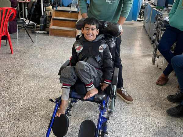Ein kleiner Junge sitzt in einem Rollstuhl und lacht. 