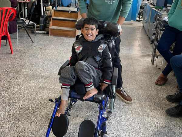 Ein kleiner Junge sitzt in einem Rollstuhl und lacht.