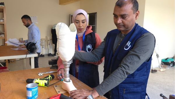Eine Frau und ein Mann mit Handicap International Westen stehen in einer Werkstatt. Der Mann hält eine Beinprothese in den Händen. 