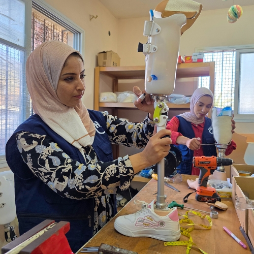 Zwei Mitarbeiterinnen und ein Mitarbeiter von Handicap International stehen an einem Tisch und bauen Beinprothesen. 