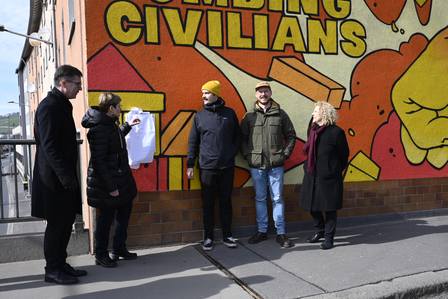 Eine Gruppe Menschen stehen vor einem Graffiti und enthüllen eine Tafel