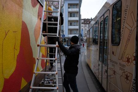 Zwei Graffiti Künstler sprühen. Hinter ihnen fährt eine Trambahn vorbei