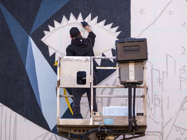 Der Künstler steht auf einer Hebebühne und sprayt eine Wand an.