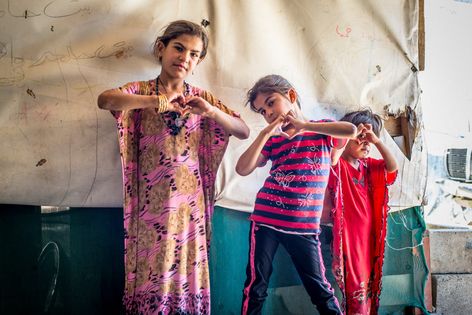 Mädchen aus Syrien formen mit den Händen ein Herz und lächeln in die Kamera.