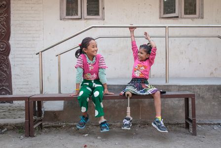 Zwei Mädchen aus Nepal lachen sich an. Sie tragen jeweils eine Beinprothese