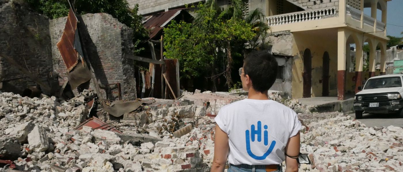 Eine HI-Mitarbeiterin steht vor vom Erdbeben zerstörten Gebäuden in Haiti