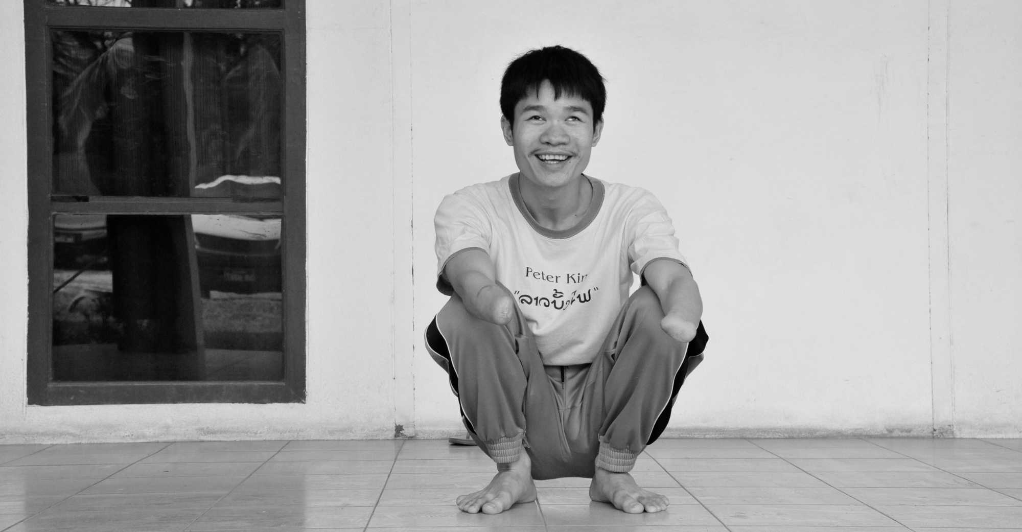 Phongsavath Manithong, Opfer von Streumunition, sitzt auf dem Boden und lacht frontal in die Kamera.