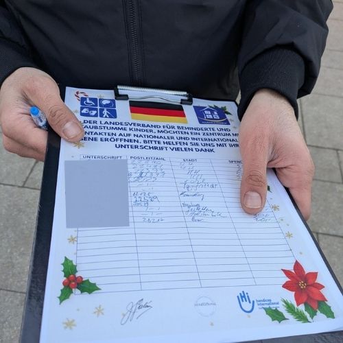 Zu sehen ist ein Foto von einem Klemmbrett, das ein falscher Spendensammler in den Händen hält. Darauf ist eine Liste mit einem Einleitungstext, verschiedenen Logos und einer deutschen Flagge.