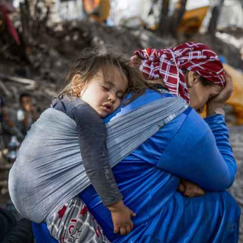 Ein kleines Kind schläft auf dem Rücken einer Frau. Im Hintergrund sieht man die Verwüstung des Erdbebens in Marokko.