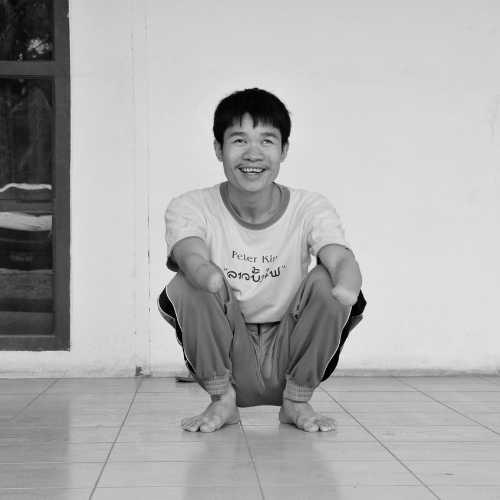Phongsavath Manithong, Opfer von Streumunition, sitzt auf dem Boden und lacht frontal in die Kamera.