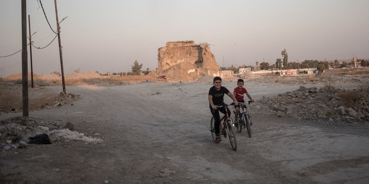 Zwei Kinder auf dem Rad vor Trümmern eines Hauses im Irak