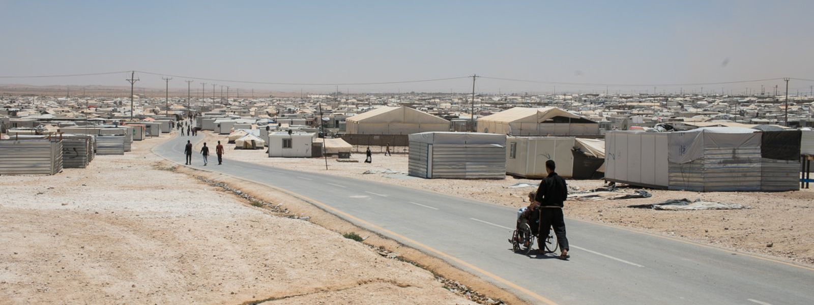 Ein Mensch im Rollstuhl wird durch ein Flüchtlingslager in der Wüste geschoben.
