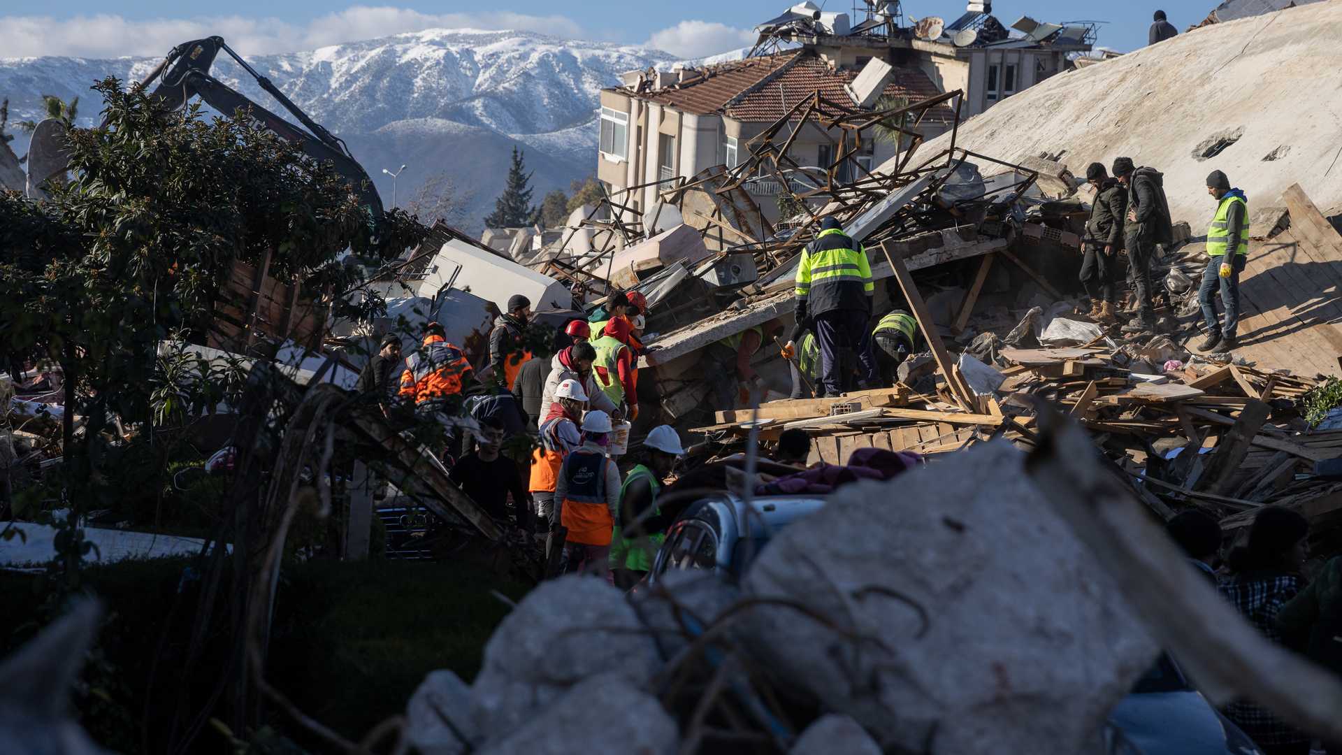 Menschen stehen vor und auf den Trümmern eines zerstörten Gebäudes.
