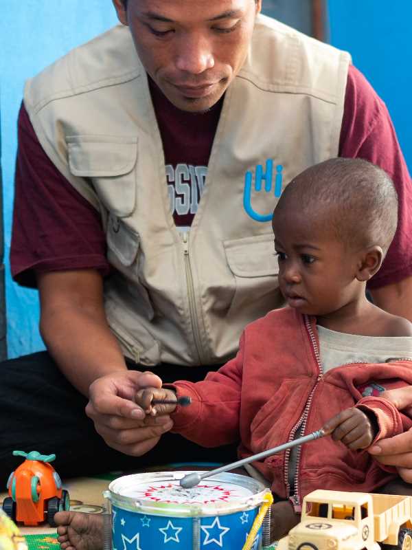 Ein Junge mit Unterernährung beim Spielen mit einem HI-Mitarbeiter