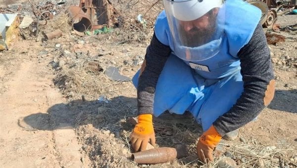 Ein Mann im Schutzanzug lehnt über einem verrosteten Kriegsrest.