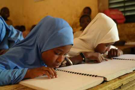 Das Mädchen Malika sitzt im Klassenzimmer und liest Brailleschrift.