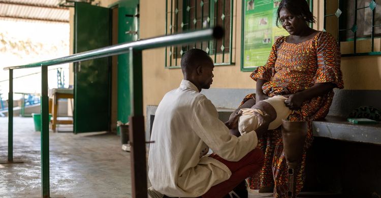 Eine Frau aus dem Tschad sitzt auf einer Bank und bekommt von einem Mitarbeiter von Handicap International eine Prothese angelegt.