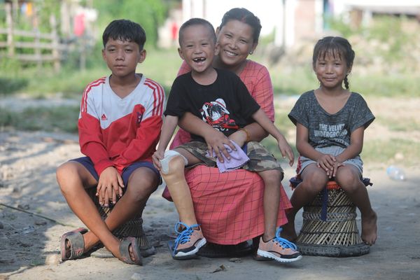 Prabin aus Nepal auf dem Schoß seiner Mutter mit seinen Geschwistern. Sie lächeln in die Kamera.