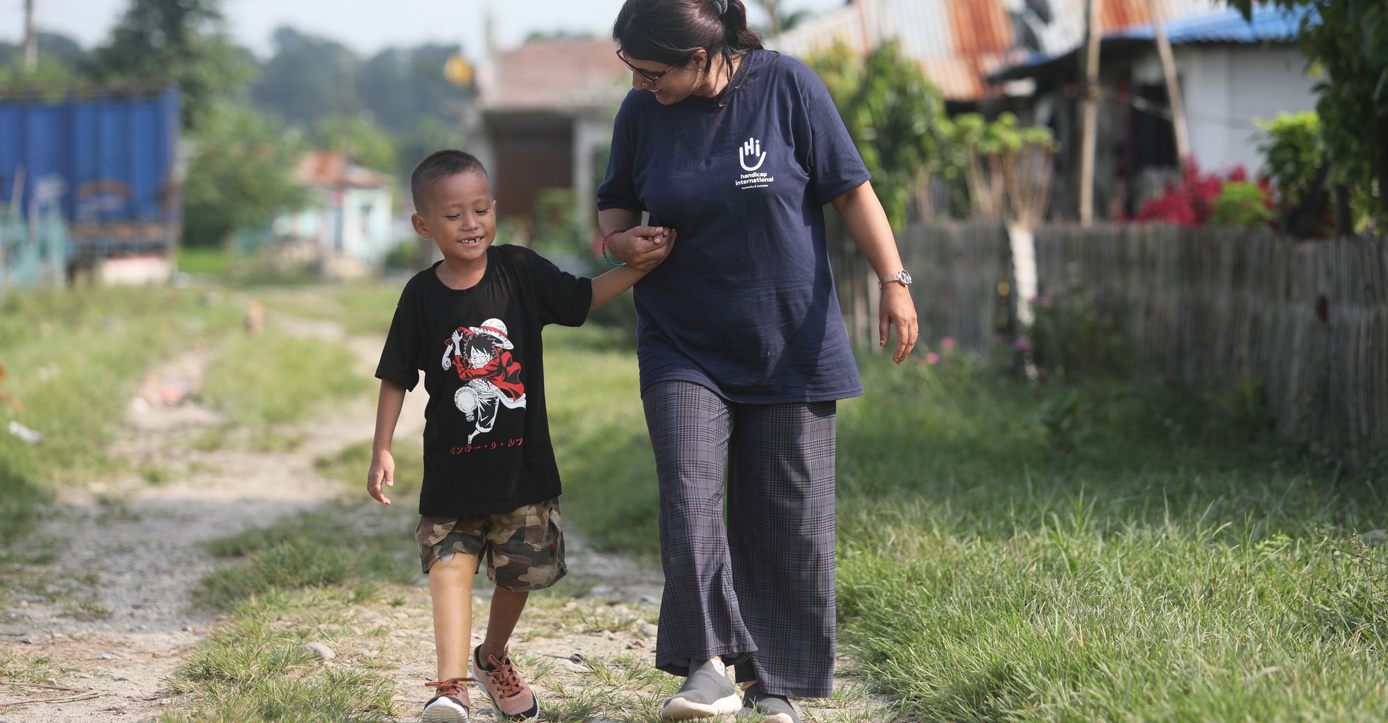 Ein Junge aus Nepal geht mit seiner Prothese an der Hand einer HI-Physiotherapeutin