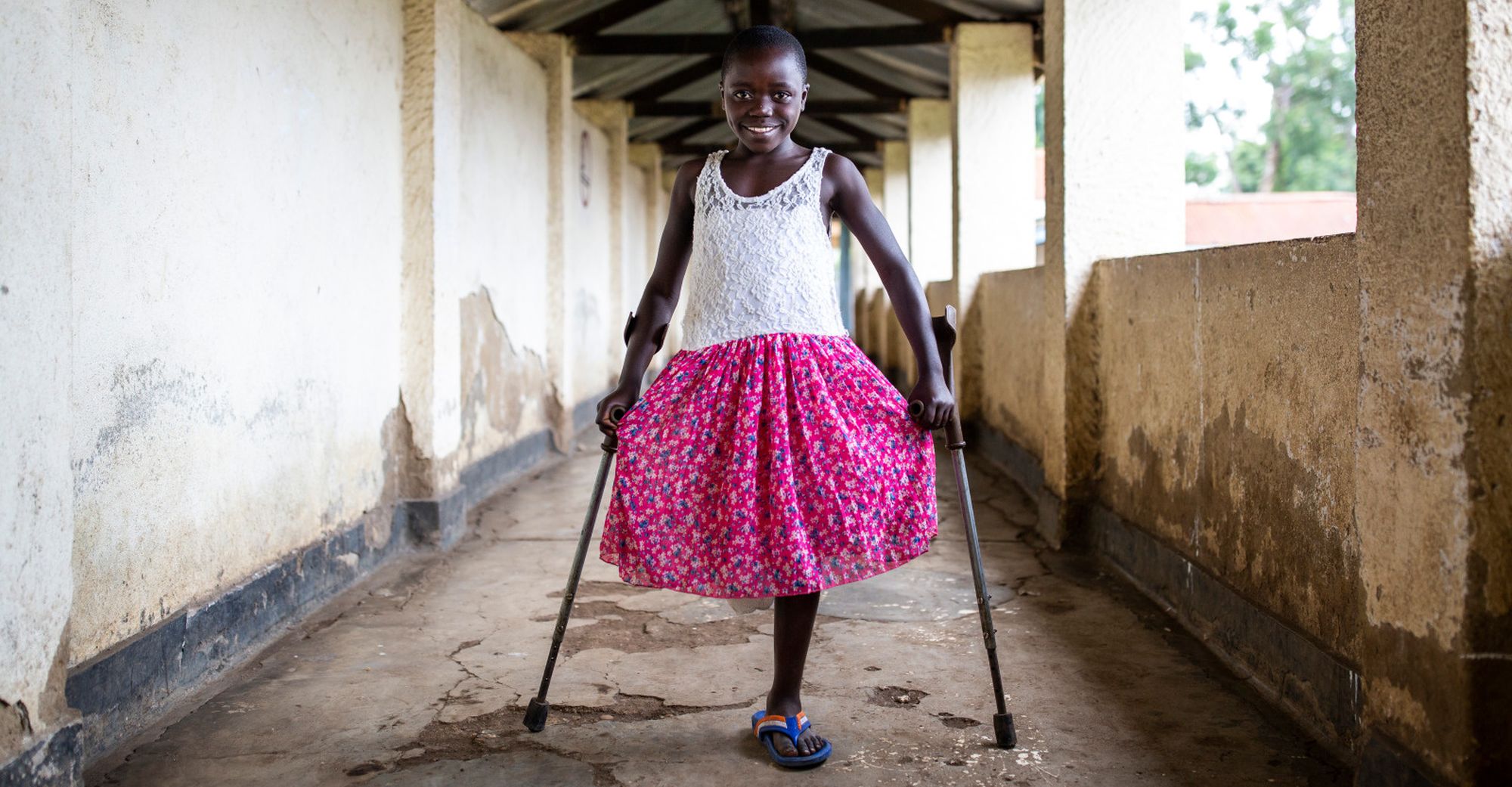 Mädchen aus der Demokratischen Republik Kongo mit pinkem Rock auf Krücken. Ihr fehlt ein Bein.