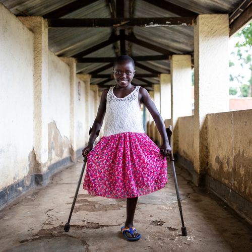 Mädchen aus der Demokratischen Republik Kongo mit pinkem Rock auf Krücken. Ihr fehlt ein Bein.