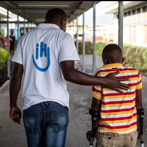 Ein HI-Mitarbeiter geht stützend neben einem Jungen mit Gehhilfen