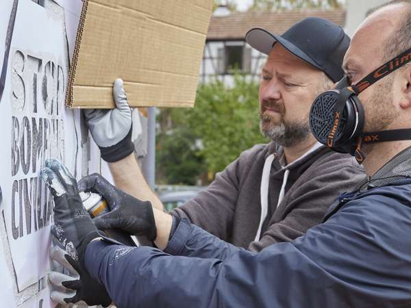 Künstler besprühen eine Wand mittels Schablonen