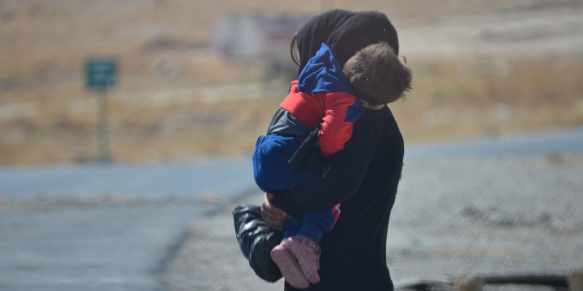 Eine Frau mit Kopftuch trägt ihr kleines Kind auf dem Arm
