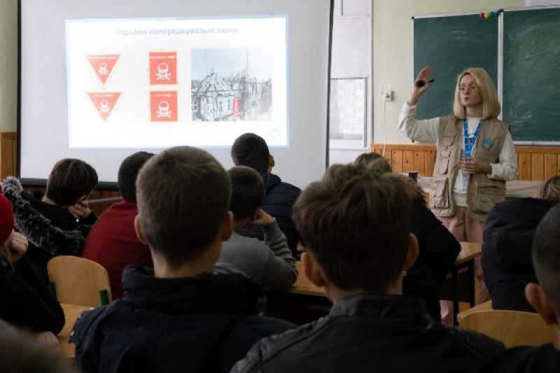 Ein Klassenzimmer, eine Frau in HI-Weste erklärt den Kindern etwas zum Thema Minen