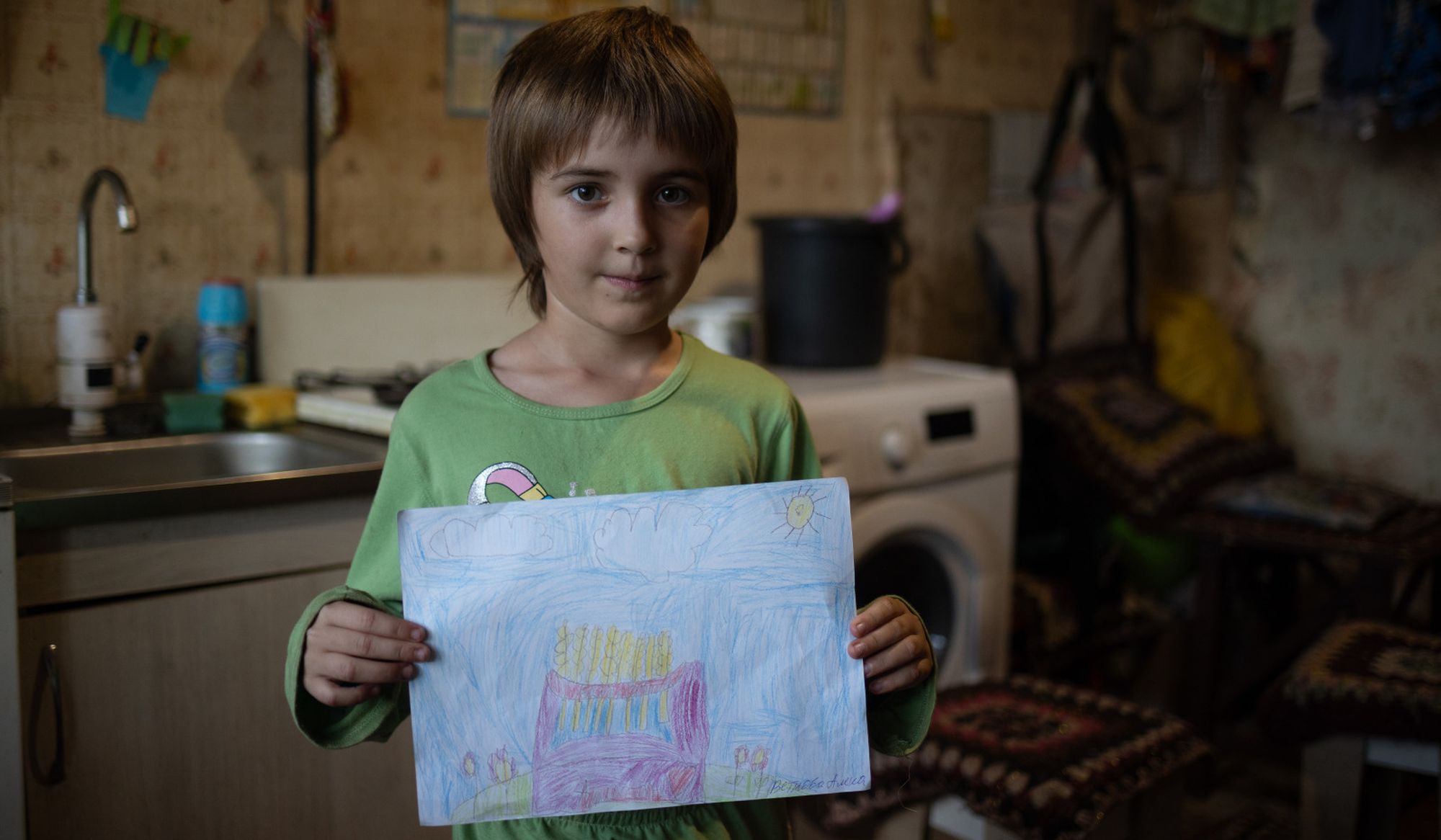 Ein junges Mädchen schaut in die Kamera und hält ein selbst gemaltes Bild hoch