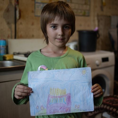 Ein junges Mädchen schaut in die Kamera und hält ein selbst gemaltes Bild hoch