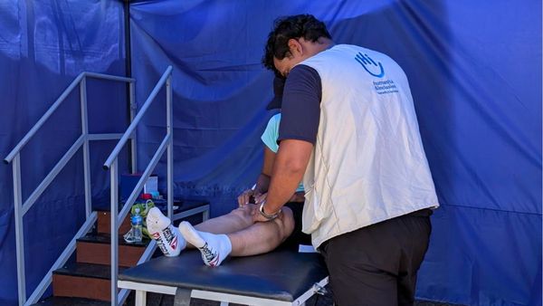 Ein Mitarbeiter von Handicap International führt mit einer auf einer Liege liegenden Person Physiotherapieübungen für die Beine durch.