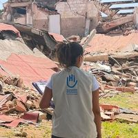Eine Frau mit HI-Weste steht vor Trümmern. Man sieht sie von hinten.